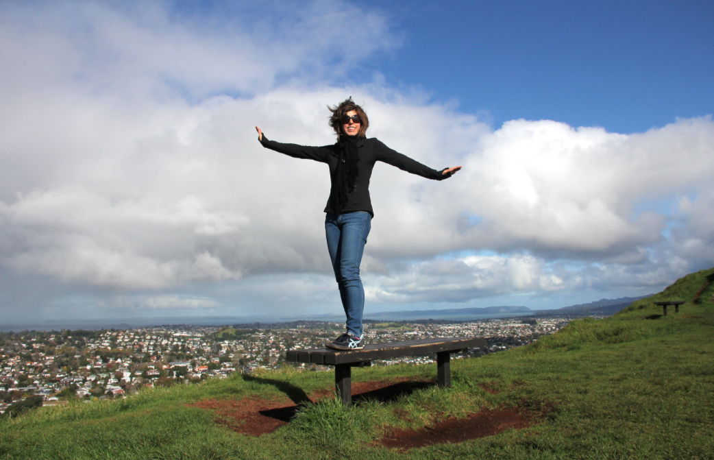 Woman stands on hilltop bench above Auckland